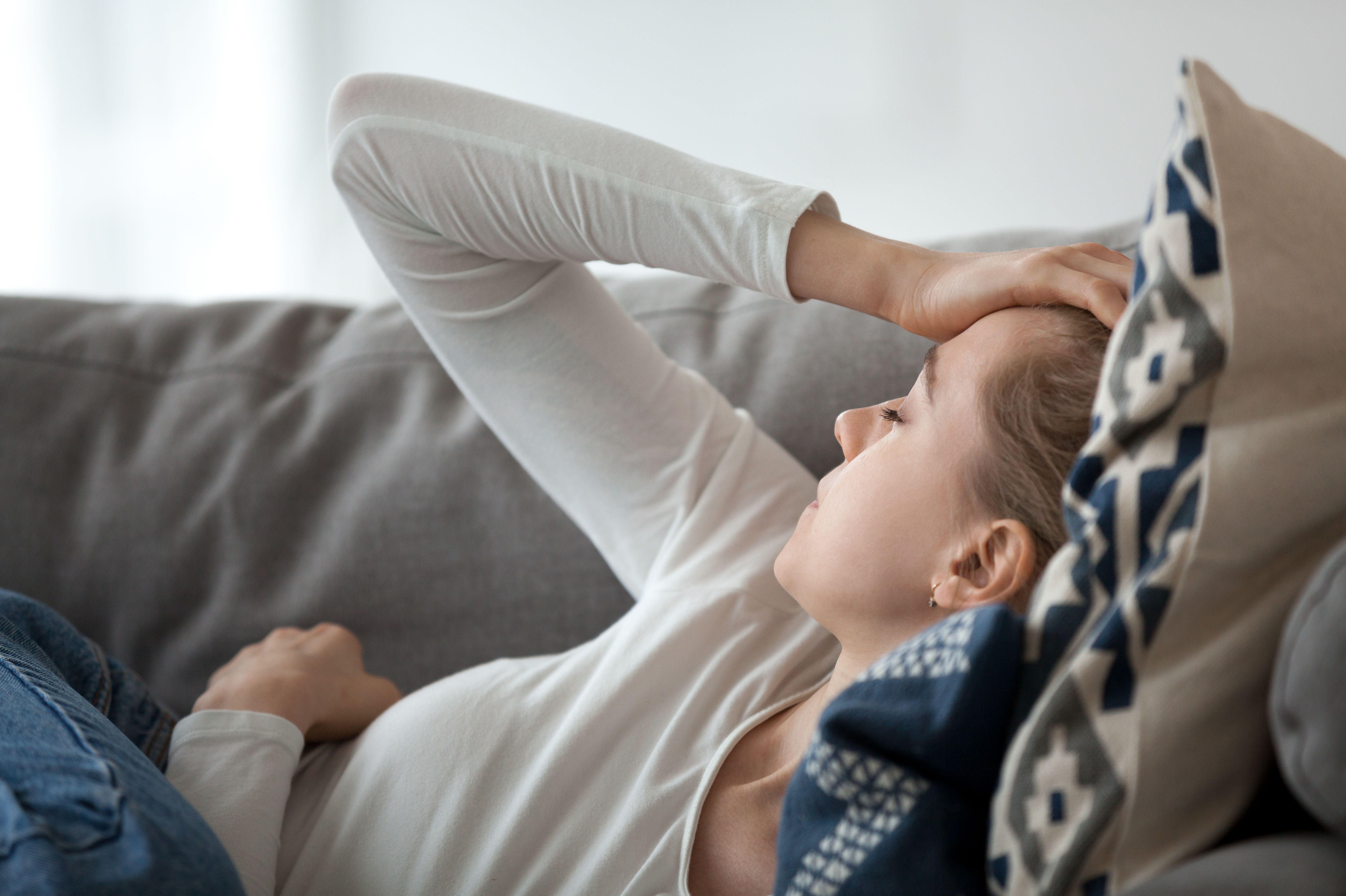 Upset depressed young woman lying on couch feeling