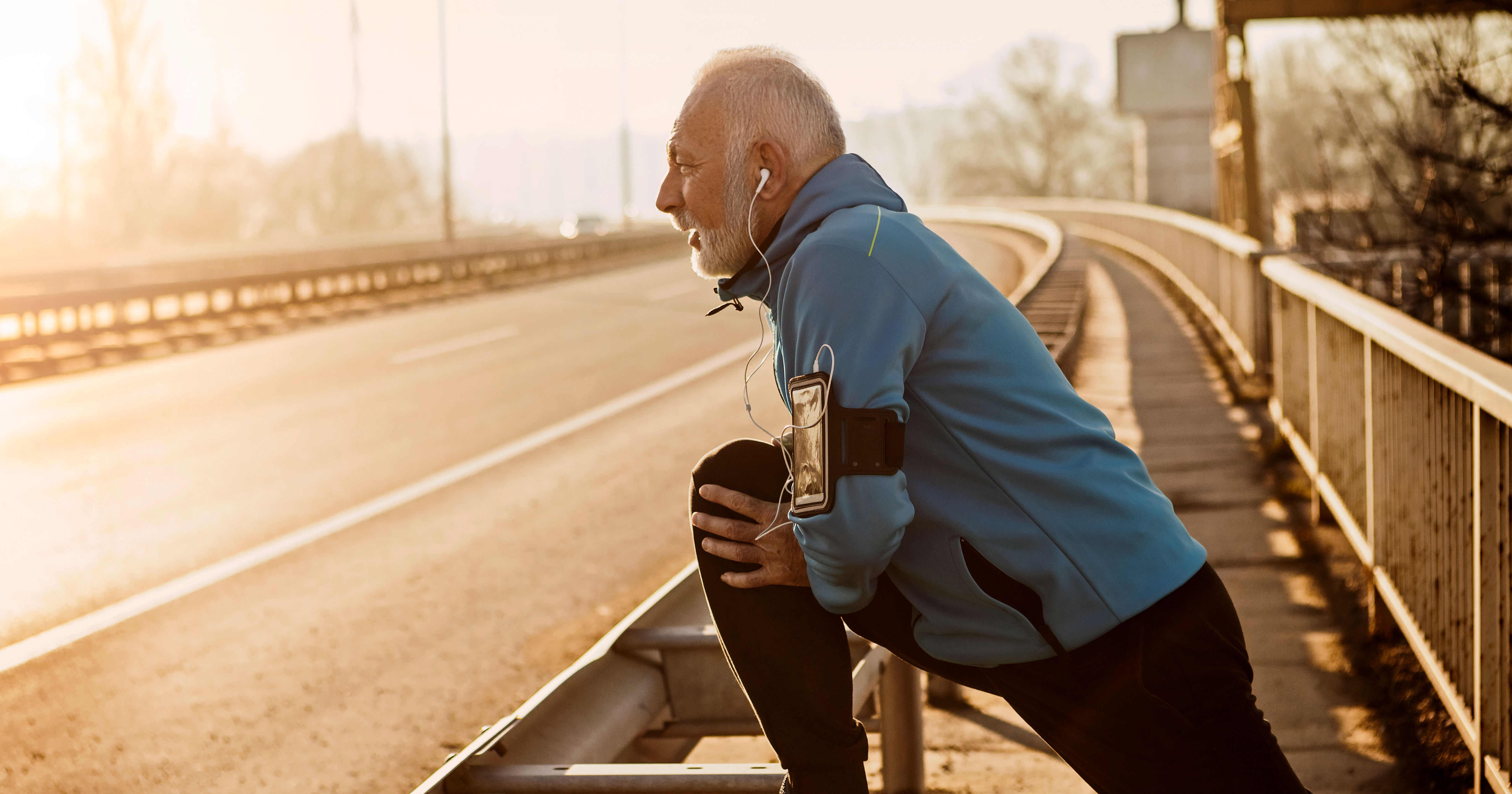 Senior man warming up for jogging on a city bridge