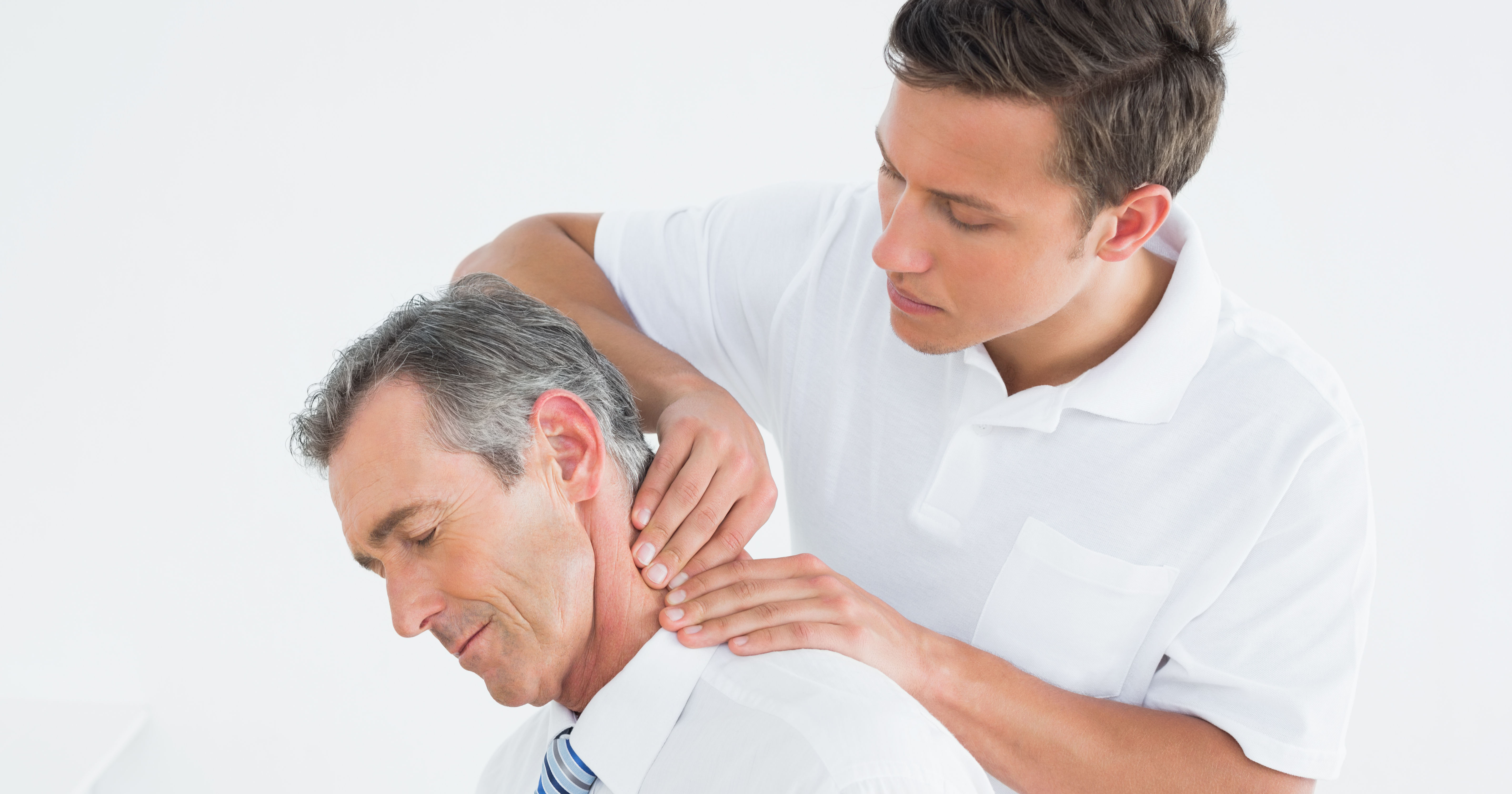 A young man is giving a neck massage to an older man in a bright, neutral setting, focusing on relaxation and therapy.