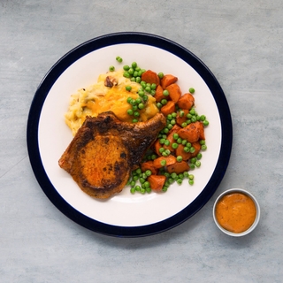 achiote pork chop with mashed potatoes, roasted carrots and green peas on a white plate