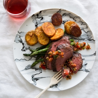 Plate with Argentinian Coulotte steak with asparagus and potatoes bravas, a glass of wine in the background 
