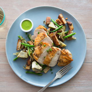 Basil chicken with artichoke hash on a blue dinner plate with basil vinaigrette in a small white dish on the side. 