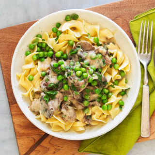 beef and mushroom stroganoff over butter noodles with fresh herbs, three drinks, a fork and spoon on a green napkin