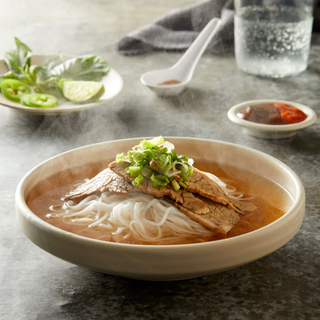 homemade beef pho with rice noodles and bean sprouts in a white soup bowl with fresh herbs and jalapeño