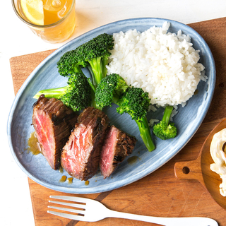 three thick slices of beef teriyaki with steamed broccoli and white rice on a blue plate on a light wooden cutting board