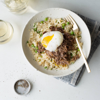 risotto with braised shredded beef and a poached egg on top in a white bowl