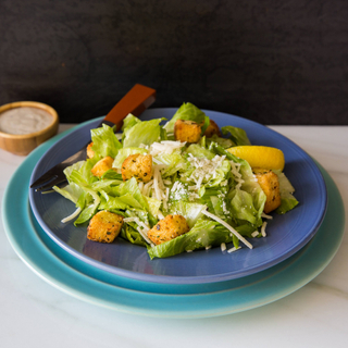 white bowl of caesar salad with garlic croutons and shaved Parmigiano-Reggiano