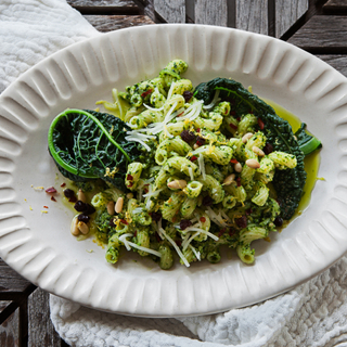 Cavatappi pasta with kale pesto and grated cheese on a white platter with a white napkin and a spoon. 