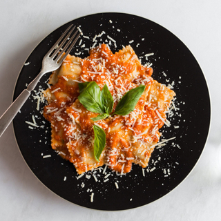 Cheese ravioli with tomato sauce and fresh basil on a black dinner plate