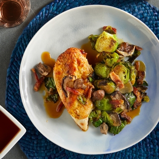 light blue plate with a roasted chicken breast and brussels sprouts with bacon on the side