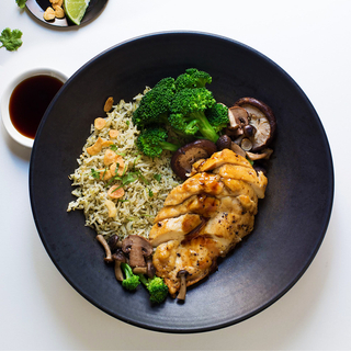 Grilled chicken breast over coconut rice with fresh broccoli on a black round dinner plate