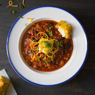 white bowl of chicken chili with beans, cheese, sour cream and a piece of cornbread