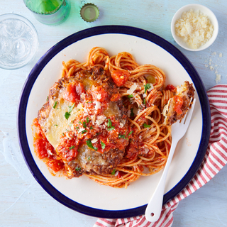 Overhead of a white and blue plate filled with spaghetti noodles and crispy chicken parmesan on a light blue background with a red and white striped napkin and a white fork in the pasta.