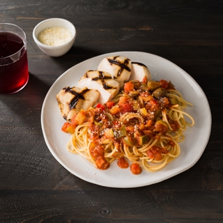 Plate of chicken cacciatore with sliced chicken and parta with a side of parmesan and a glass of red wine 