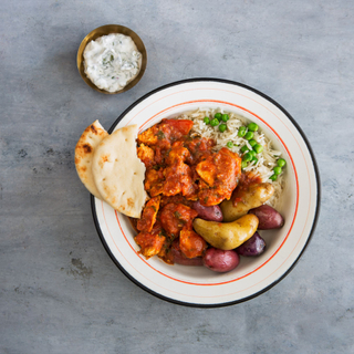 chicken vindaloo in a white bowl with fingerling potatoes, rice and peas and naan bread