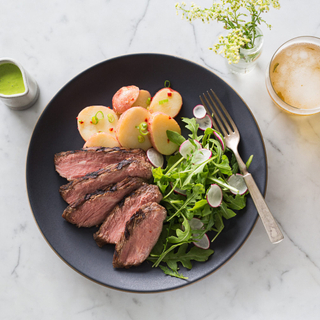 sliced chimichurri steak with potato salad and green and radish salad ona black plate