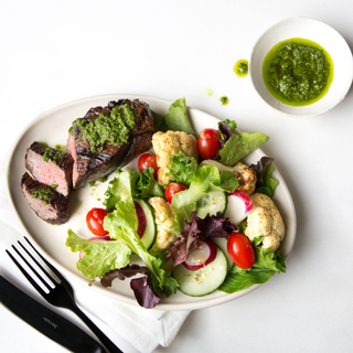 chimichurri tri-tip grilled with salad of tomatoes, lettuce and cauliflower on a white platter