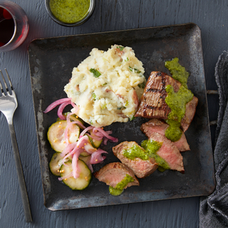 sliced chimichurri steak with mashed potatoes and cucumber salad