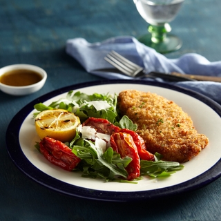 breaded chicken milanese with a salad of tomatoes, lettuce and lemon on a white dinner plate