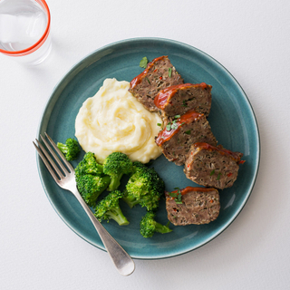 two slices of classic meatloaf on a blue square plate with cooked peas and mashed potatoes