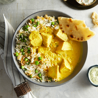 Coconut chicken curry with basmati white rice and green peas in a bowl with a side of naan bread and a blue striped napkin in a napkin ring on the side. 