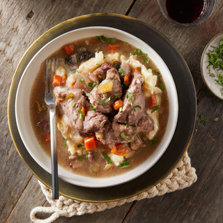 white bowl of coq au vin with mashed potatoes on a black plate on a dark wooden background