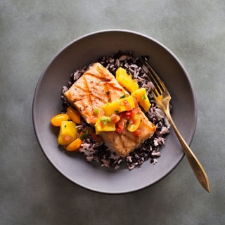 roasted salmon fillet with mango salsa and wild rice in a black bowl