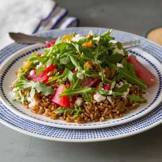 Round blue rimmed bowl with Farro & Chioggia Beet Salad topped with arugula with a fork showing