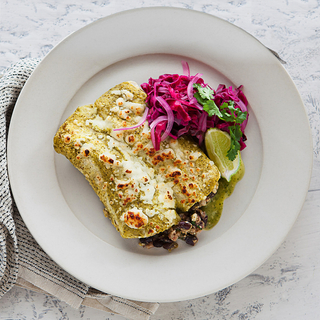 two farro enchiladas with red cabbage slaw and cheese on a white plate with a striped napkin on the side