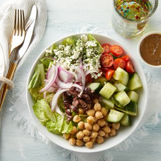 Greek salad in a white bowl with carefully arranged tomatoes, cucumber, chick pesas, red onion and feta cheese