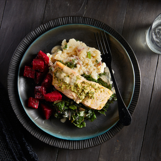 Black and blue layered dinner plates with gremolata roasted salmon, roasted chopped red beets, mashed potatoes and sauteed greens with a black fork. 