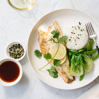 sea bass fillet with a lemon slice, baby bok choy, green beans and white rice on a white dinner plate with a fork