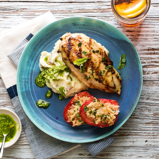 Grilled chicken breast with pesto and mashed potatoes with parmesan roasted tomato halves on a bright teal plate on a wooden background. 