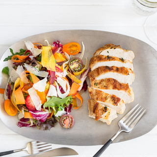 grilled chicken breast on a plate next to a colorful raw vegetable salad
