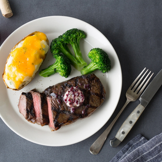 new york strip steak grilled and sliced on a white plate with twice baked potato and three steamed broccoli florets