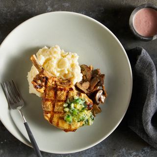 Round white plate with truffled mashed potatoes, wild mushrooms and a grilled pork chop with a fork on the plate. 