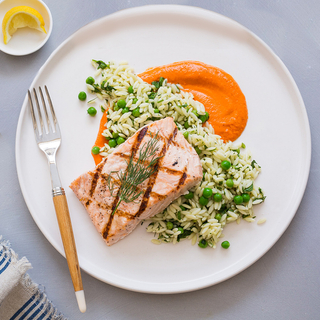 grilled salmon fillet over orzo pasta salad with fresh peas and romesco puree on a white dinner plate