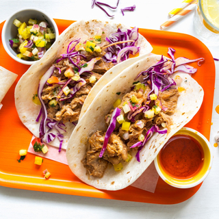 Two hawaiian pulled pork tacos with purple cabbage slaw in flour tortillas on an orange plate