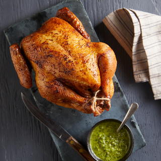 Whole rotisserie chicken on a black serving tray with a bowl of chimichurri sauce with a spoon