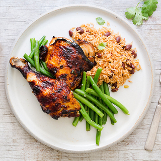 honey lime chicken thigh and leg on a plate with green beans and dirty rice and beans