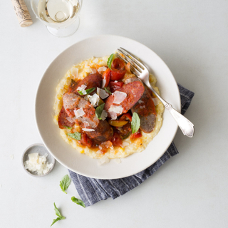 polenta with italian sausages and peppers in tomato sauce in a white bowl with a fork