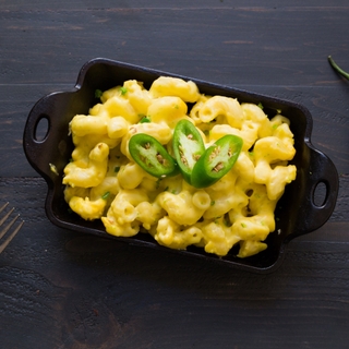 Jalapeno mac and cheese, garnished with fresh jalapeno, in a cast iron rectangular dish on a dark surface 