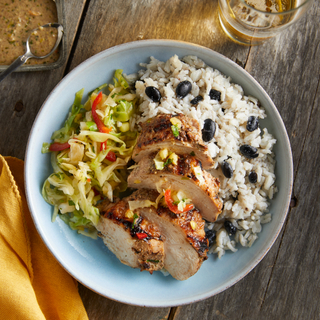 Jerk chicken breast sliced into four slices with white rice and black beans and pineapple slaw on a wooden table. 