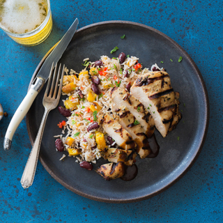 jerk chicken with roasted plantains and rice and beans on a white dinner plate