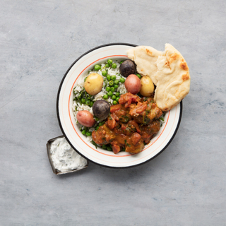 black plate with steamed white rice and lamb vindaloo with carrots and peas and fresh naan