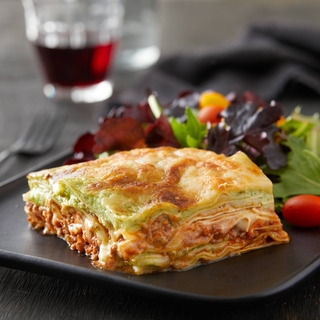 slice of pesto lasagna on a black plate with a side salad and a glass of red wine.