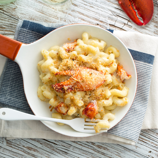 cast iron skillet with lobster mac and cheese and a wooden bowl of salad on the side