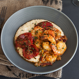 Blue dinner bowl with low country-style shrimp and grits topped with roasted tomatoes on a blue background with kitchen twine on the table. 