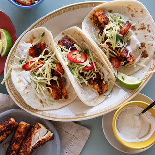 three mahi mahi fish tacos with flour tortillas and slaw on a white plate