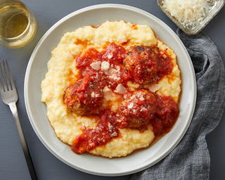 Polenta with three meatballs and tomato sauce on a round white plate with a grey linen napkin on the side. 